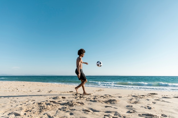 Uomo atletico che dà dei calci alla palla sulla spiaggia