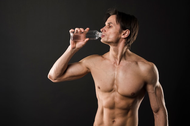 Uomo atletico senza camicia che beve dalla bottiglia di acqua