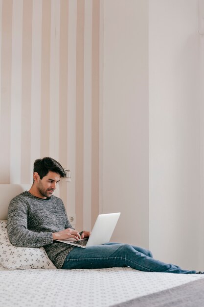 Uomo attraente che per mezzo del computer portatile sul letto