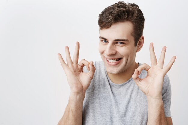 Uomo attraente con gli occhi azzurri, sorridendo con gioia che mostra segno giusto con entrambe le mani, felice dopo l'incontro con la sua ragazza isolata. Espressioni ed emozioni facciali umane