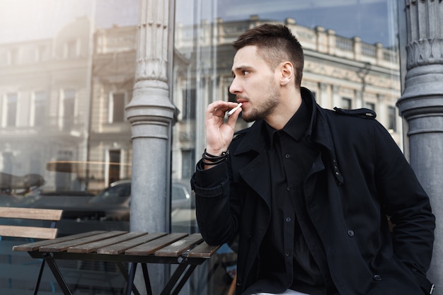 Uomo attraente in abiti neri si sedette per avere una sigaretta.