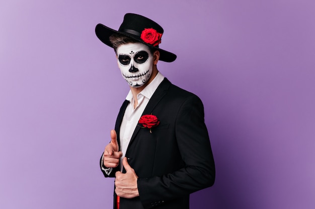 Uomo attraente nella maschera di Halloween pone in abito classico su sfondo viola.