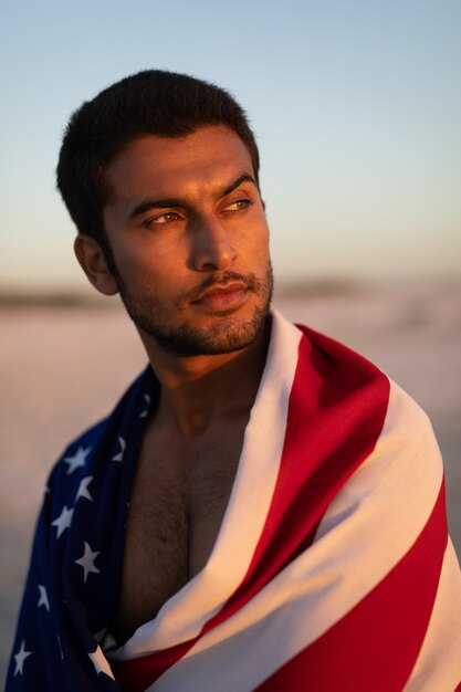 Uomo avvolto in bandiera americana in piedi sulla spiaggia