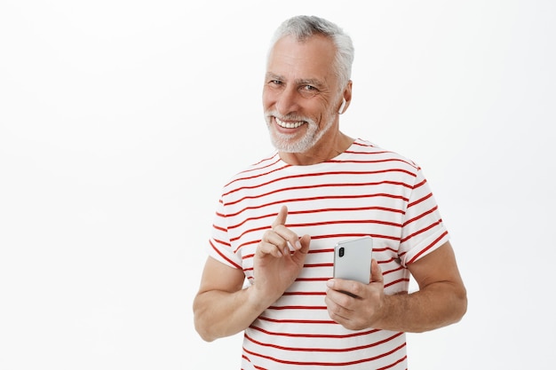 Uomo barbuto adulto sorridente bello utilizzando smartphone e auricolari wireless