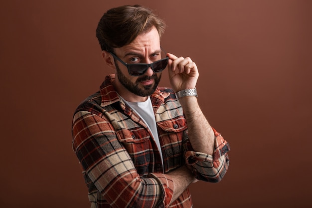 Uomo barbuto alla moda bello hipster emotivo con espressione faccia buffa su marrone