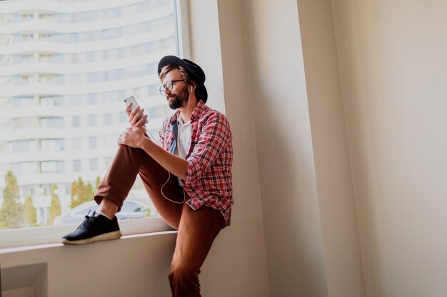 Uomo barbuto alla moda in camicia a scacchi luminosa che installa nuova applicazione mobile