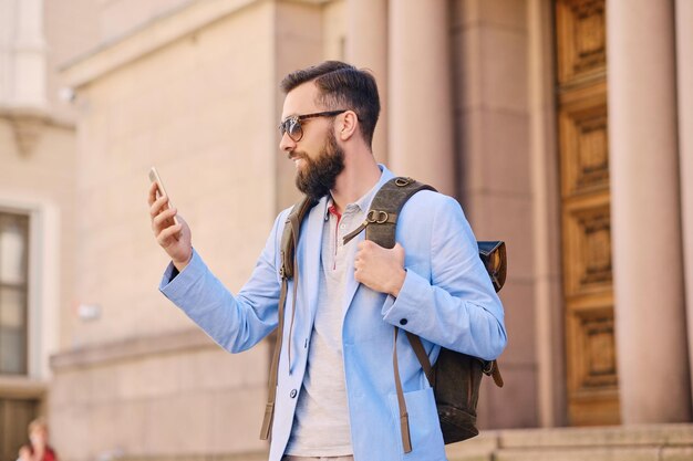 Uomo barbuto alla moda in una giacca blu tramite smartphone.