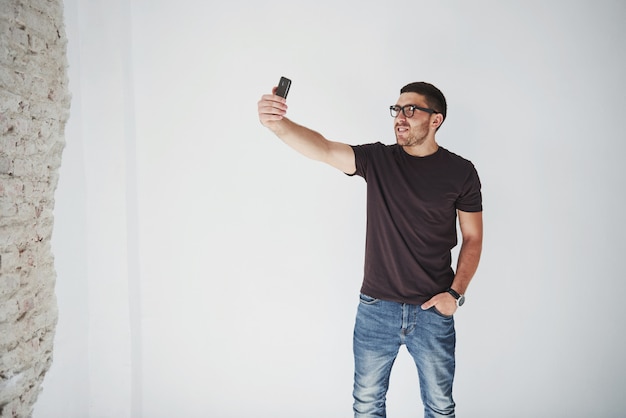 Uomo barbuto allegro che fa selfie sullo smartphone e sulla parete bianca