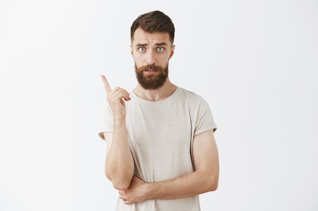 Uomo barbuto barbuto bello che posa contro il muro bianco