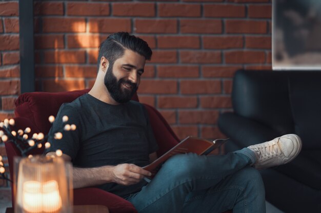 Uomo barbuto bello ritratto che indossa abbigliamento casual, seduto in un moderno loft sedia rossa