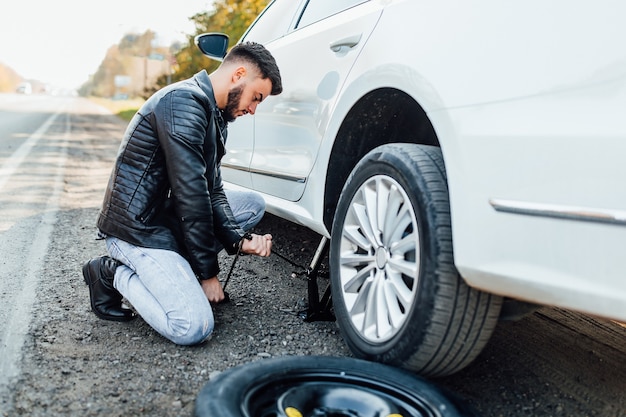 Uomo barbuto che cambia la gomma della sua auto