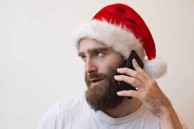 Uomo barbuto che indossa il cappello di Santa e parla al telefono