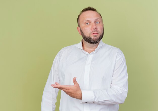 Uomo barbuto che indossa una camicia bianca che punta con il braccio di lato confuso in piedi sopra la parete leggera