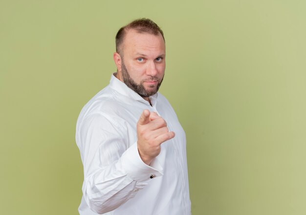 Uomo barbuto che indossa una camicia bianca che punta con il dito indice in piedi sopra la parete leggera