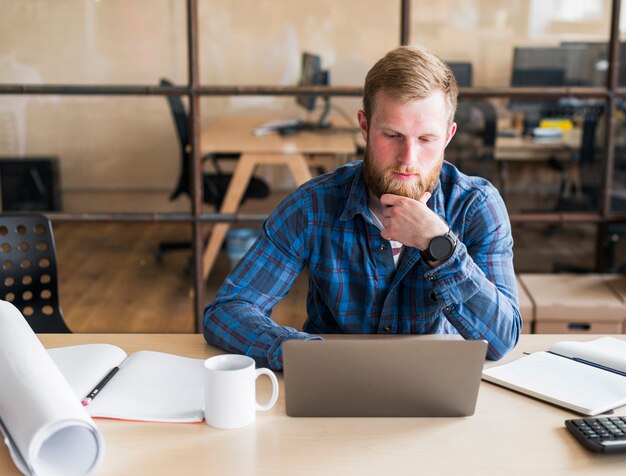 Uomo barbuto che lavora al computer portatile sul posto di lavoro