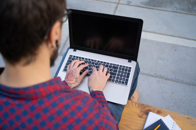 Uomo barbuto che si siede sul banco di legno, digitando sul computer portatile