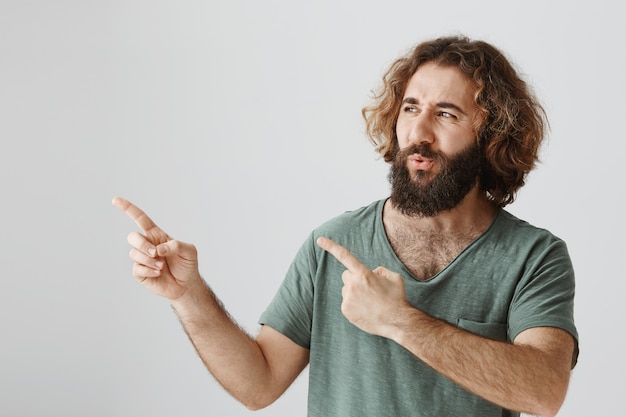 Uomo barbuto confuso e preoccupato che guarda e punta a sinistra