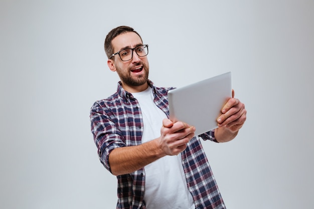 Uomo barbuto felice in occhiali che gioca sul computer tablet