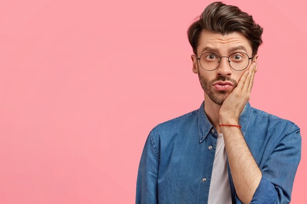 Uomo barbuto in camicia di jeans e occhiali rotondi