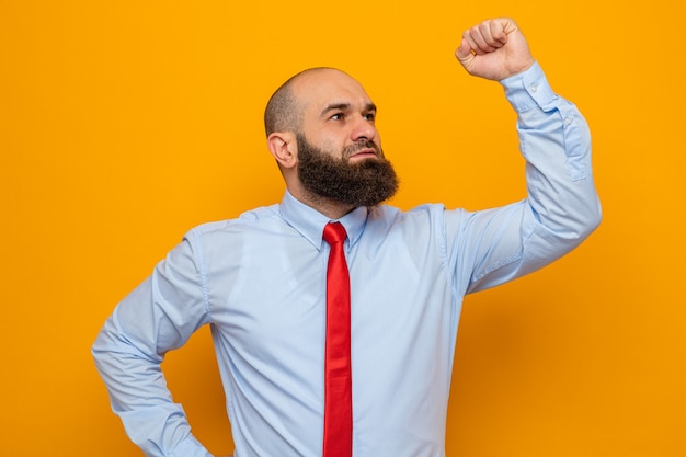 Uomo barbuto in cravatta rossa e camicia che guarda da parte felice e fiducioso alzando il pugno come un vincitore