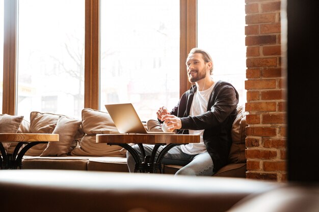 Uomo barbuto nella caffetteria con il computer portatile