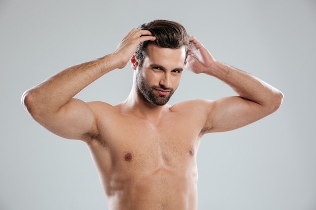 Uomo barbuto nudo affascinante che posa e che tocca i suoi capelli