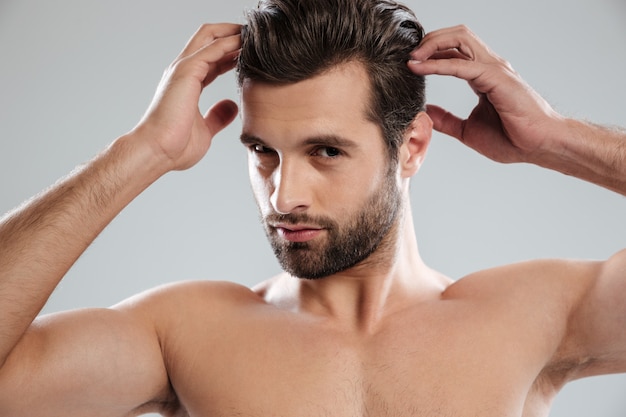 Uomo barbuto nudo affascinante che posa e che tocca i suoi capelli