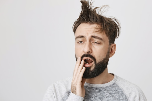 Uomo barbuto stanco con capelli disordinati che sbadiglia al mattino