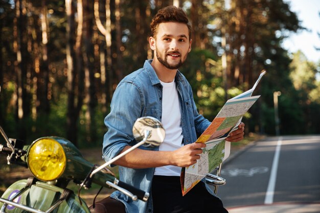 Uomo barbuto vicino al motorino che esamina mappa all'aperto.