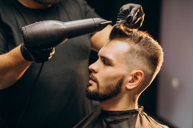 Uomo bello ad un negozio di barbiere che disegna capelli