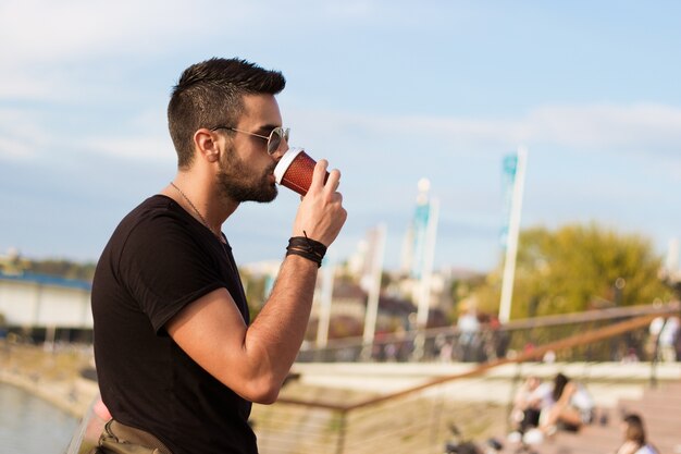 Uomo bello all&#39;aperto a bere il caffè. Con gli occhiali da sole, un ragazzo con la barba. Effetto Instagram.