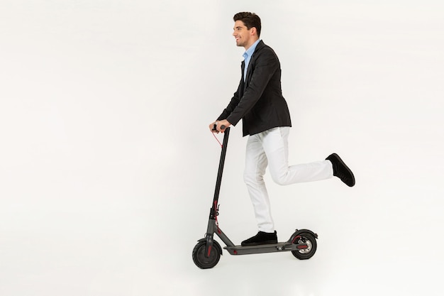 Uomo bello che cavalca uno scooter elettrico isolato su sfondo bianco per studio