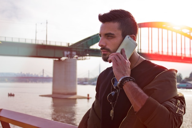 Uomo bello che comunica sul telefono all&#39;aperto. Con giacca, occhiali da sole, un ragazzo con la barba. Effetto Instagram