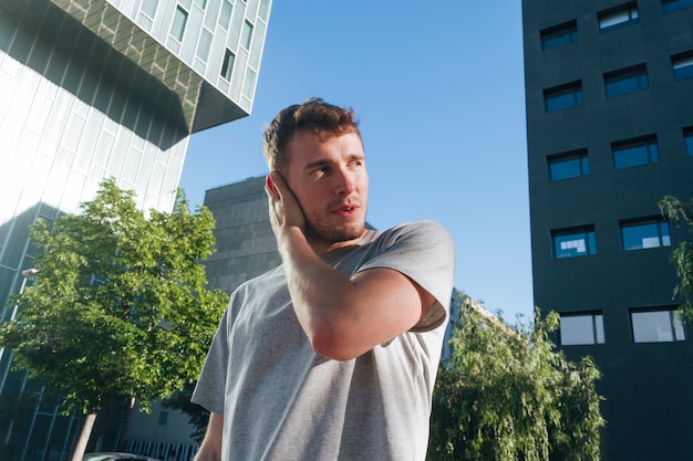 Uomo bello che copre il suo orecchio di mano che sta davanti alla costruzione moderna