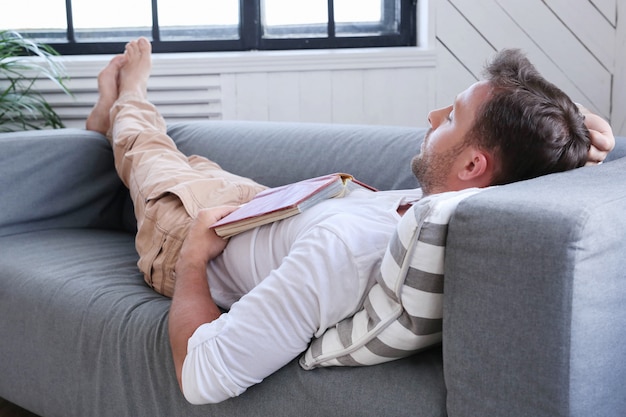 Uomo bello che dorme sul divano con un libro