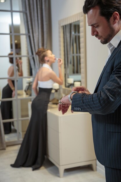 Uomo bello che guarda il suo orologio e donna che fa il trucco dietro