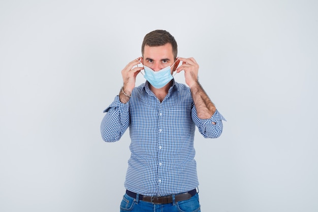 Uomo bello che indossa la maschera in camicia, jeans e che sembra serio, vista frontale.