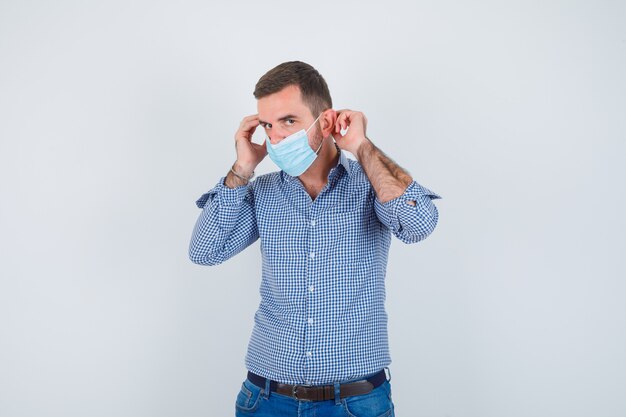 Uomo bello che indossa la maschera in camicia, jeans e che sembra serio, vista frontale.