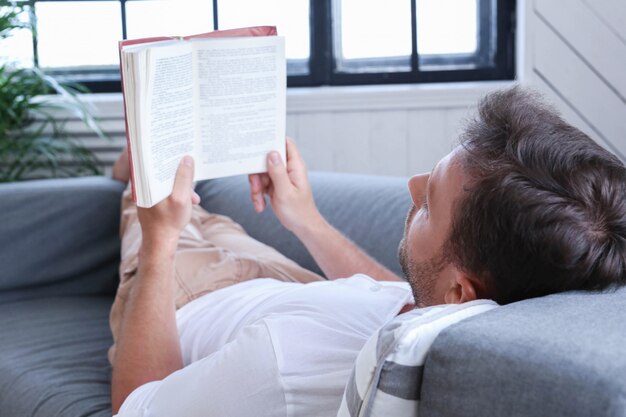 Uomo bello che legge un libro nel sofà