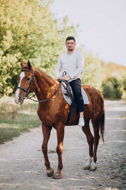 Uomo bello che monta un cavallo nella foresta