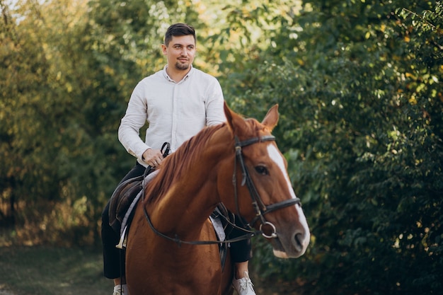 Uomo bello che monta un cavallo nella foresta