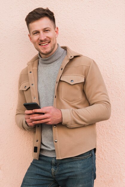 Uomo bello che posa mentre tenendo smartphone