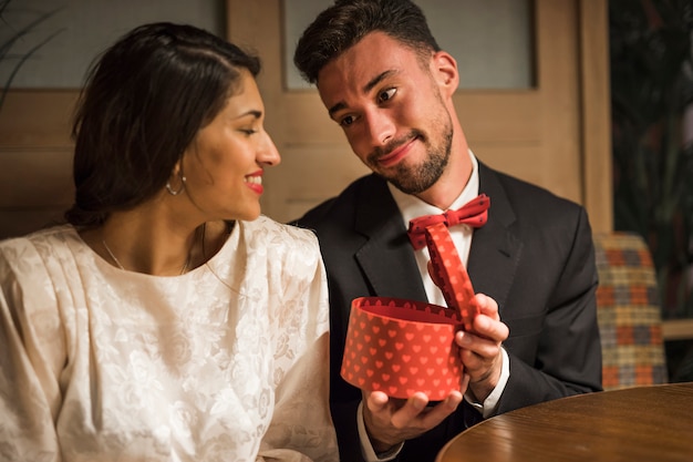 Uomo bello che presenta il contenitore di regalo alla giovane donna felice