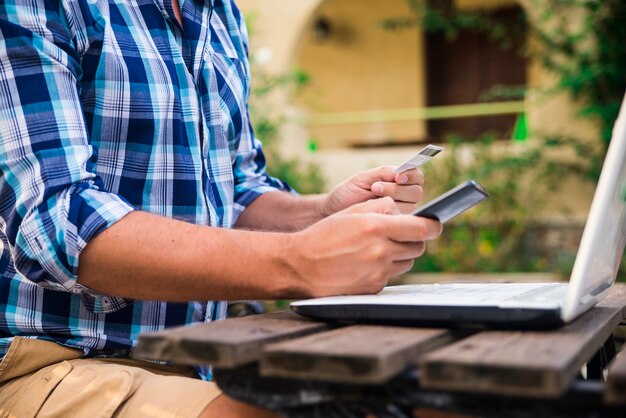 Uomo bello che si distende nel suo giardino usando il computer portatile per fare acquisti in una giornata di sole