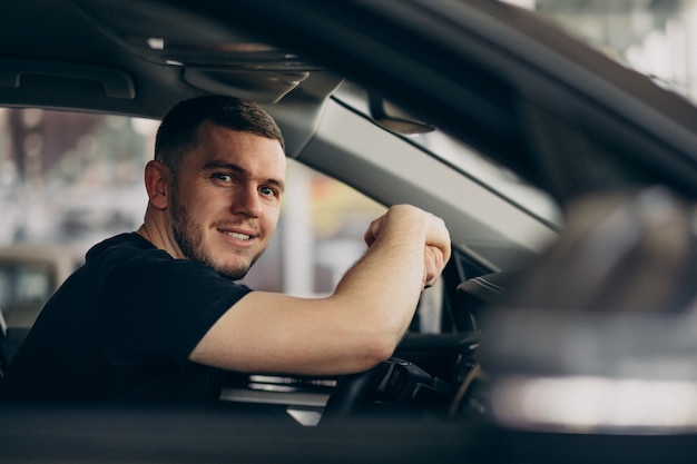 Uomo bello che si siede in automobile e che lo prova