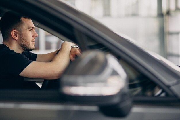 Uomo bello che si siede in automobile e che lo prova