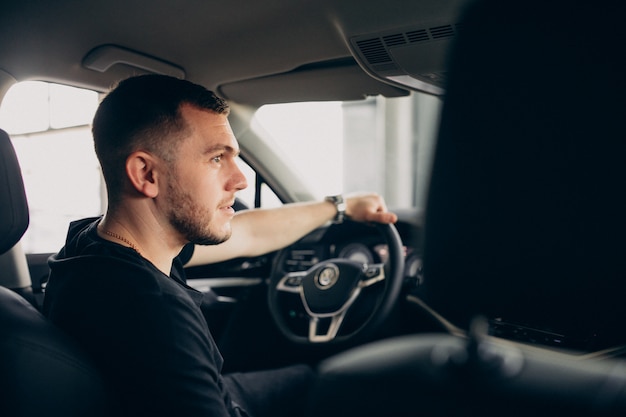 Uomo bello che si siede in automobile e che lo prova