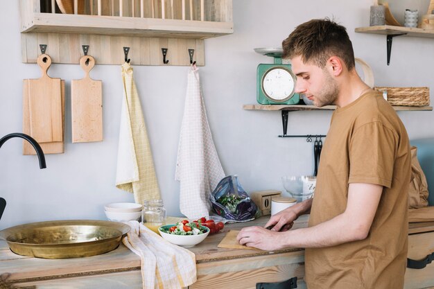 Uomo bello che taglia le verdure a pezzi sul tagliere per produrre insalata