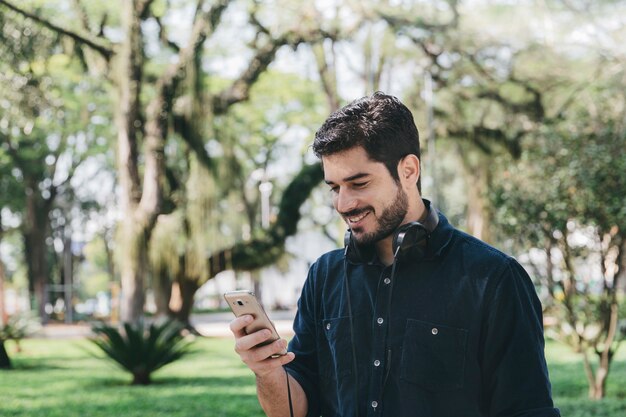 Uomo bello che utilizza telefono in natura