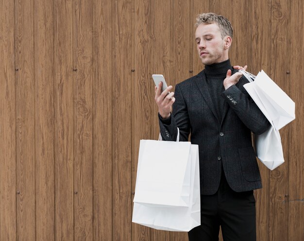 Uomo bello con i sacchetti della spesa che esamina smartphone